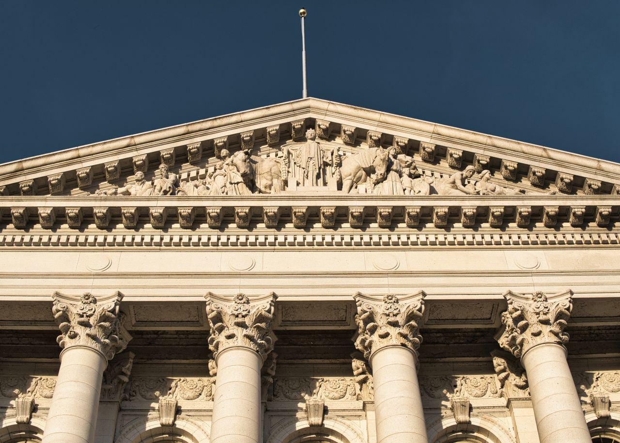 Close-up of neoclassical architecture in Madison, Wisconsin, showcasing ornate columns and pediment under a clear blue sky.