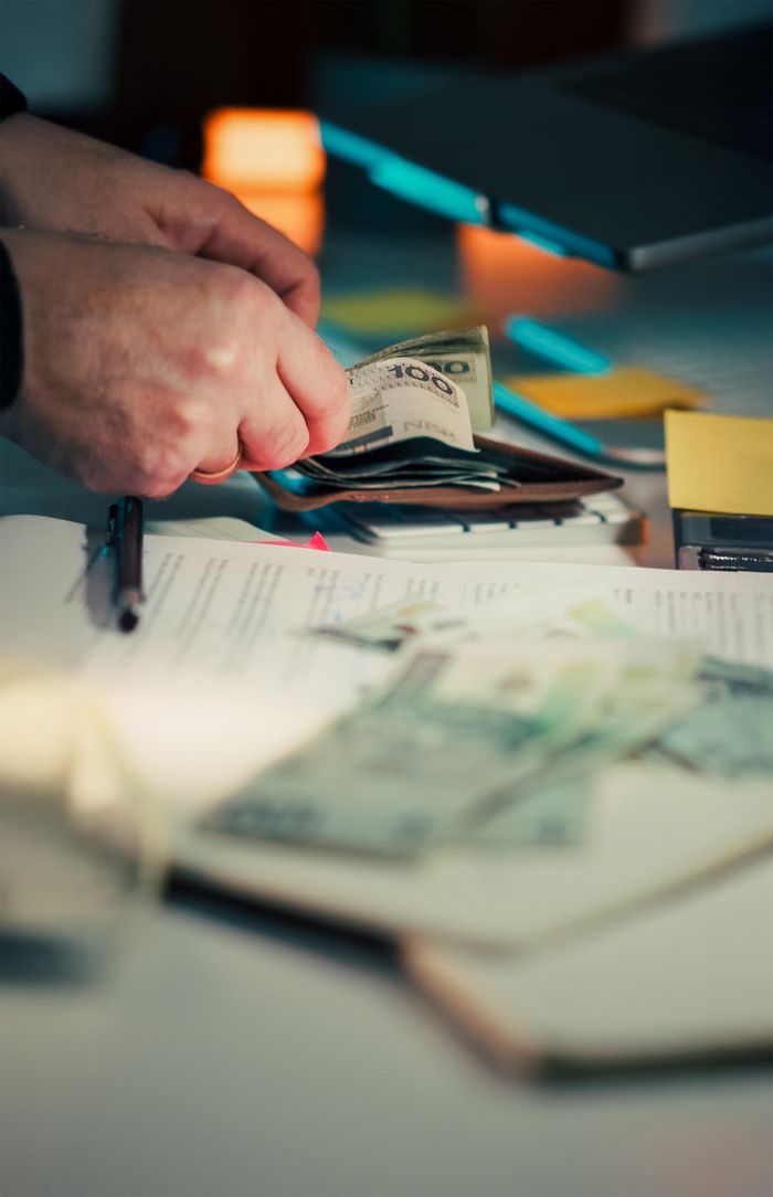 Close-up of hands counting cash next to a wallet and documents on a desk.